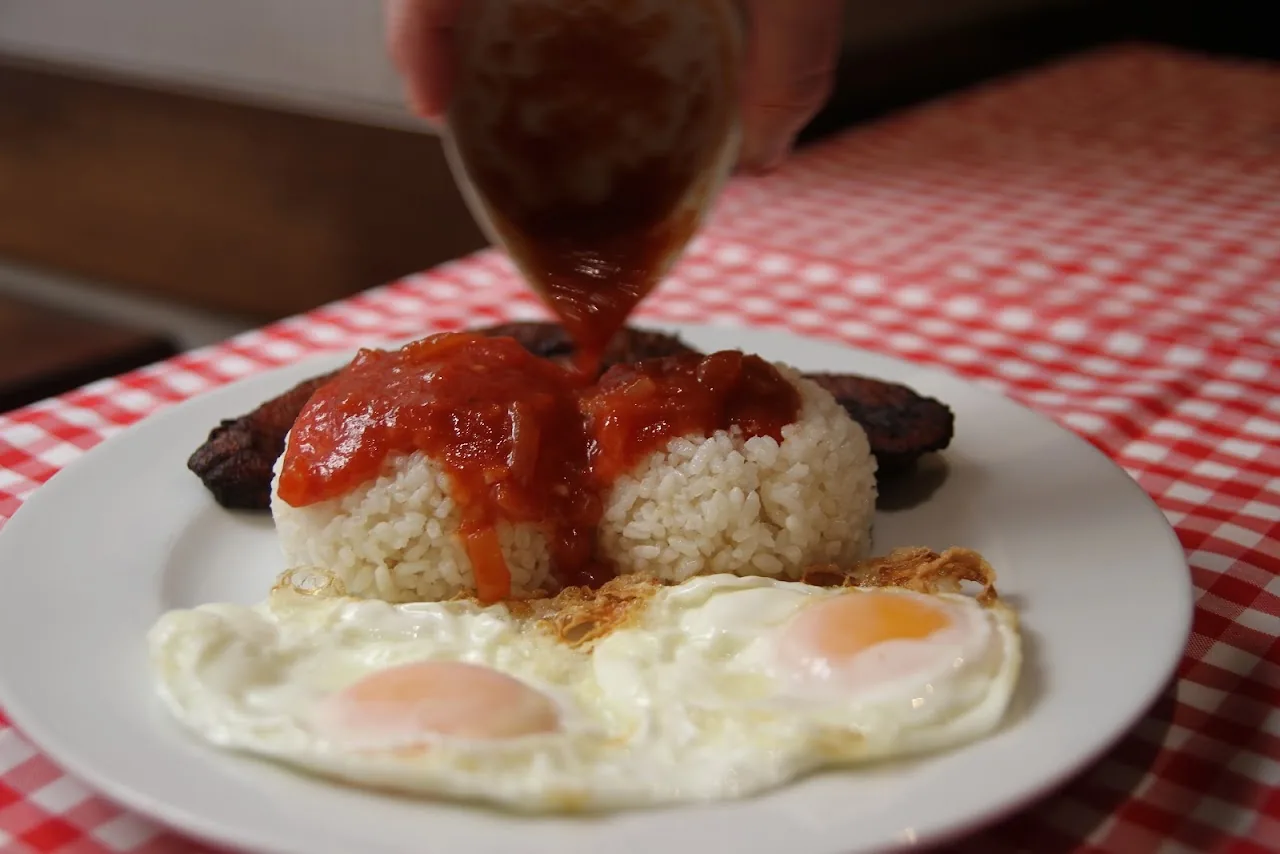 White rice topped with a fried egg and sausage, with tomato sauce being poured over it