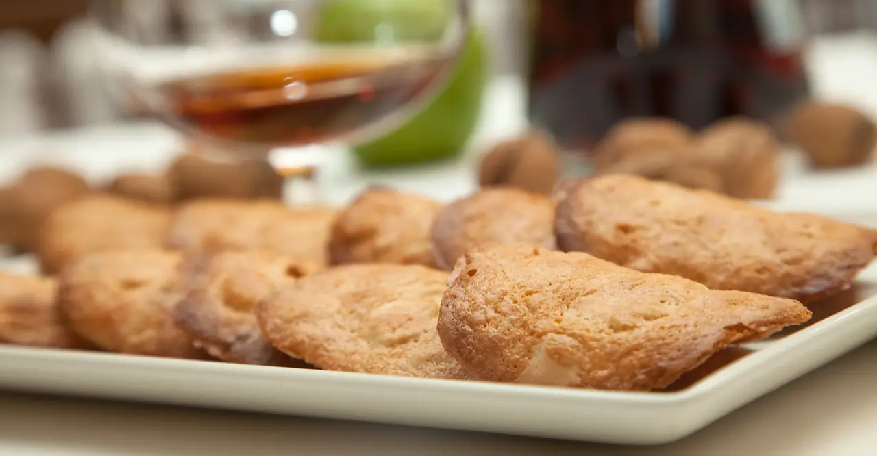 White plate of golden fried pastry cookies with a glass of amber liqueur behind them