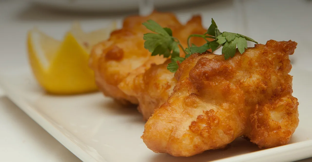 Golden battered fish pieces with a lemon wedge and parsley on a white plate