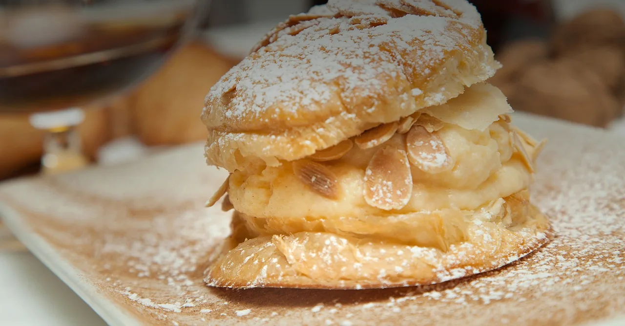 A layered puff pastry dessert topped with sliced almonds and icing sugar