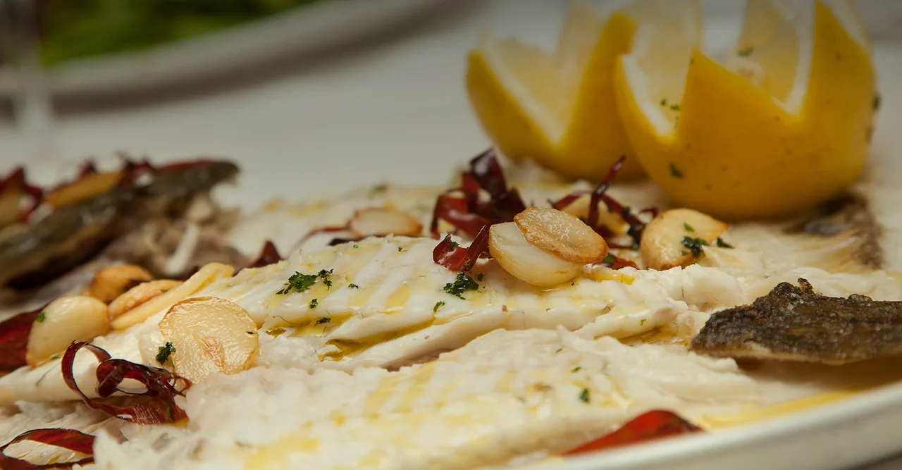 A fish fillet with lemon wedges and garlic on a white plate
