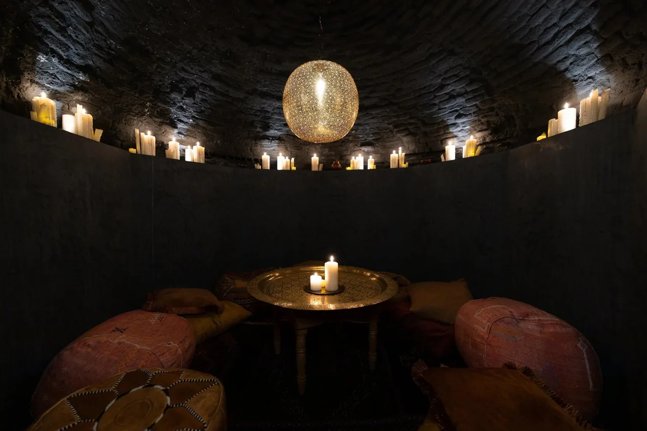 A round dark room with a small candlelit table and pink seating under a glowing ceiling